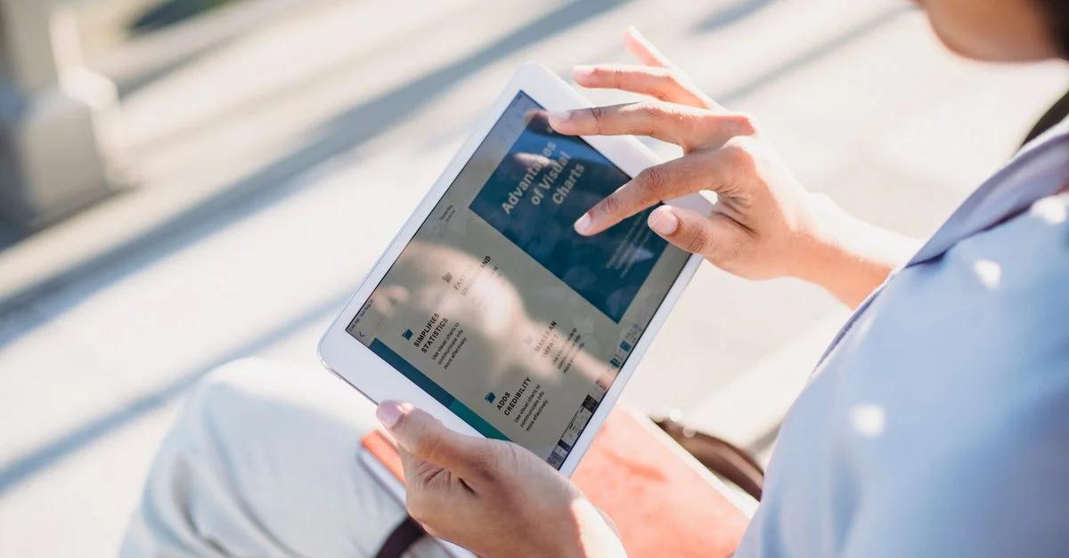 Une femme utilisant une tablette à l'extérieur, consultant à la lumière naturelle.